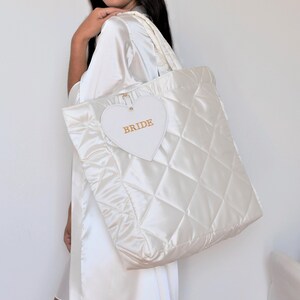 White quilted satin bridal tote bag with “Bride” detail, displayed with detachable zip pouch, elegant wedding accessory.