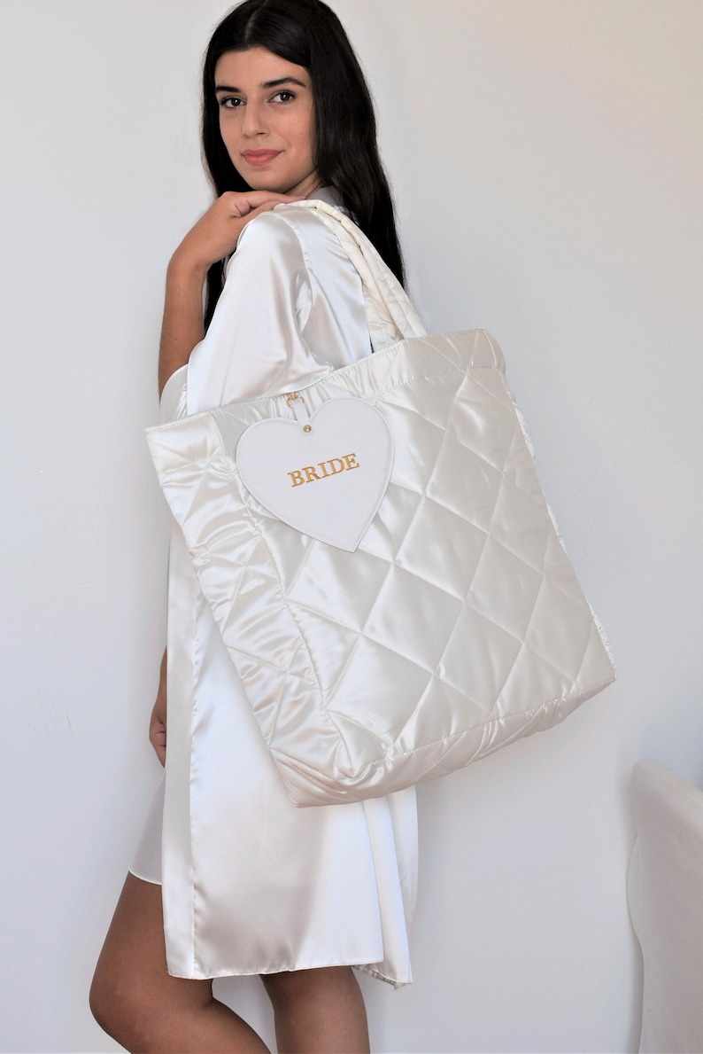 White quilted satin bridal tote bag with “Bride” detail, displayed with detachable zip pouch, elegant wedding accessory.