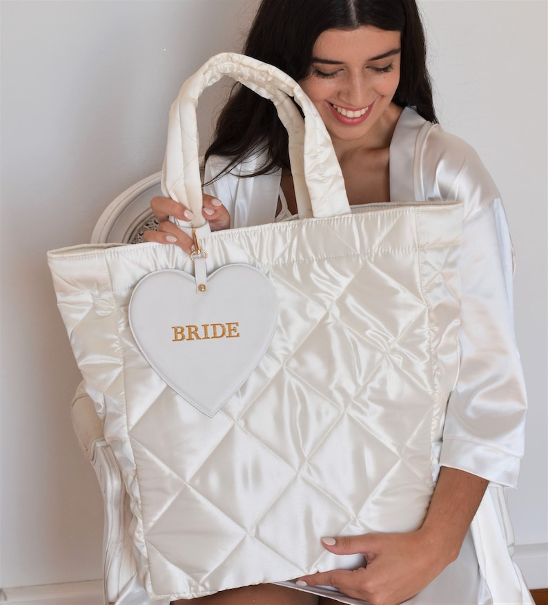 White quilted satin bridal tote bag with “Bride” detail, displayed with detachable zip pouch, elegant wedding accessory.