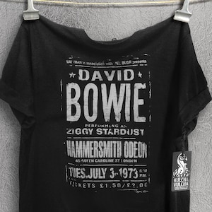 Peut inclure: T-shirt noir avec une impression blanche d'une affiche de concert pour David Bowie se produisant en tant que Ziggy Stardust au Hammersmith Odeon le 3 juillet 1973. L'affiche comprend le texte "AA! MAN in association with EL BUSH presents", "Tickets £1.50/£2.00", et "KULCHA VULCHA".