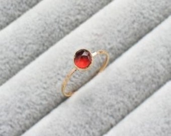 Puede incluir: Un delicado anillo de oro con una gema roja redonda. El anillo tiene una banda fina y texturizada. La gema muestra un degradado de tonos rojos, realzando la elegancia del anillo. Una joya sencilla pero elegante.