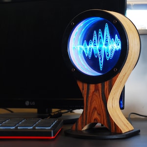 May include: A unique, handcrafted audio visualizer with a wooden base and frame. The circular display shows a blue sound wave pattern. The base is made of dark wood, and the frame is a light-colored wood.