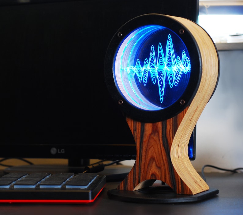 May include: A unique, handcrafted audio visualizer with a wooden base and frame. The circular display shows a blue sound wave pattern. The base is made of dark wood, and the frame is a light-colored wood.