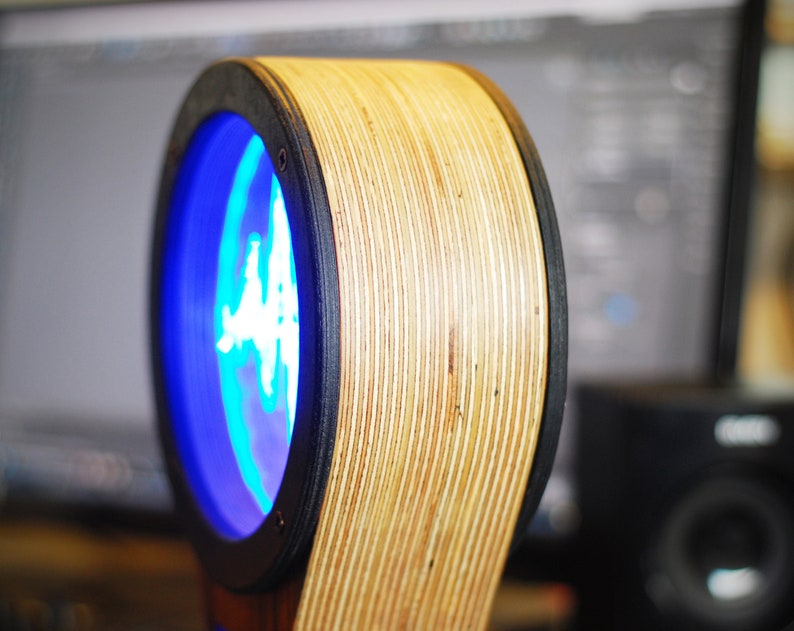 May include: A unique, circular wooden speaker with a blue illuminated center. The speaker has a layered wood design with a black trim. The speaker is designed to be a modern and stylish addition to any home audio setup.