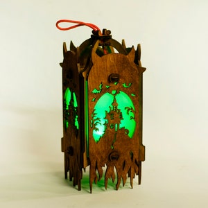 May include: A wooden lantern with a green glow, featuring a silhouette of a haunted house and bats. The lantern has a red string for hanging.