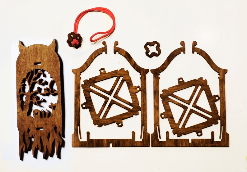 May include: A wooden craft kit for building a spooky Halloween lantern. The kit includes a pre-cut wooden base, a wooden frame, and a decorative wooden panel with a spooky tree and ghost design. The kit also includes a red string and a small wooden star.