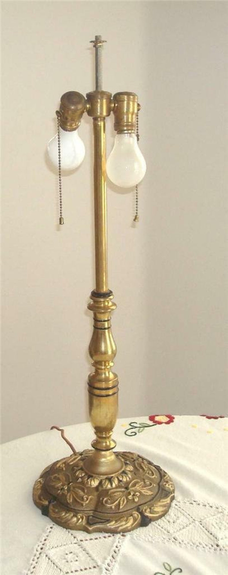 May include: A gold table lamp with two white light bulbs and a decorative base with floral designs.