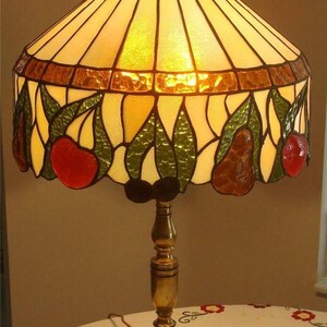May include: A stained glass table lamp with a brass base. The lampshade features a pear and leaf design with shades of green, brown, and red.