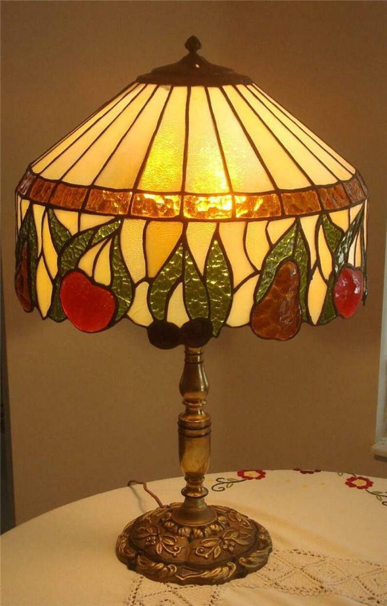 May include: A stained glass table lamp with a brass base. The lampshade features a pear and leaf design with shades of green, brown, and red.