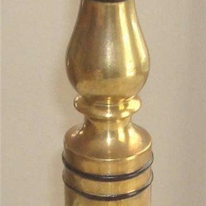 May include: A gold-toned lamp base with black accents. The base is a tall, slender cylinder with a bulbous middle section. The base has a decorative, ornate design at the bottom.