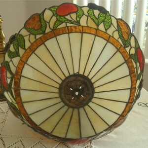 May include: A stained glass lampshade with a white, cream, and brown background. The shade has a floral design with red, orange, and green accents. The shade is round and has a metal ring around the top.