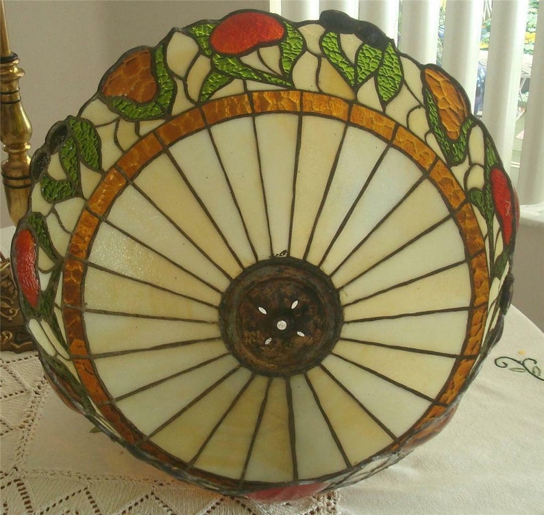 May include: A stained glass lampshade with a white, cream, and brown background. The shade has a floral design with red, orange, and green accents. The shade is round and has a metal ring around the top.