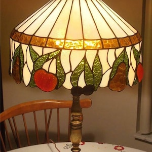 May include: A stained glass lamp with a white, gold, green, and red design. The lamp has a gold base with a floral design.