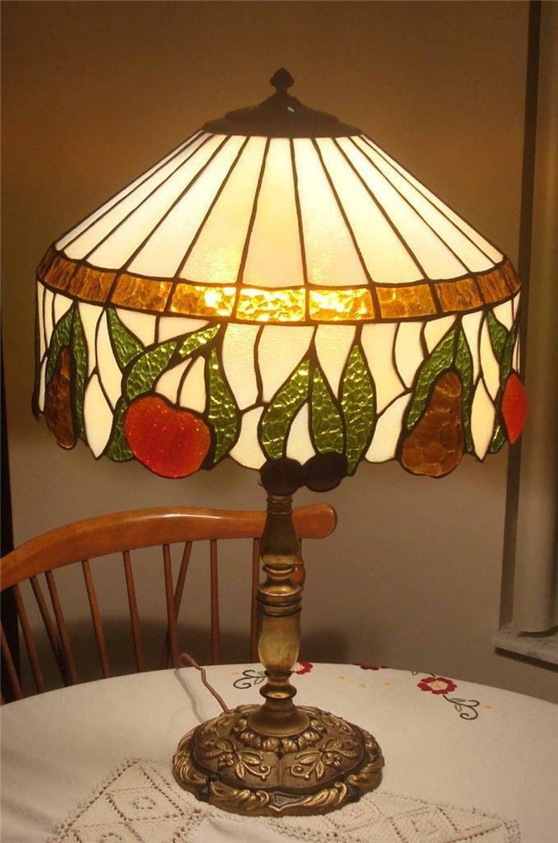 May include: A stained glass lamp with a white, gold, green, and red design. The lamp has a gold base with a floral design.