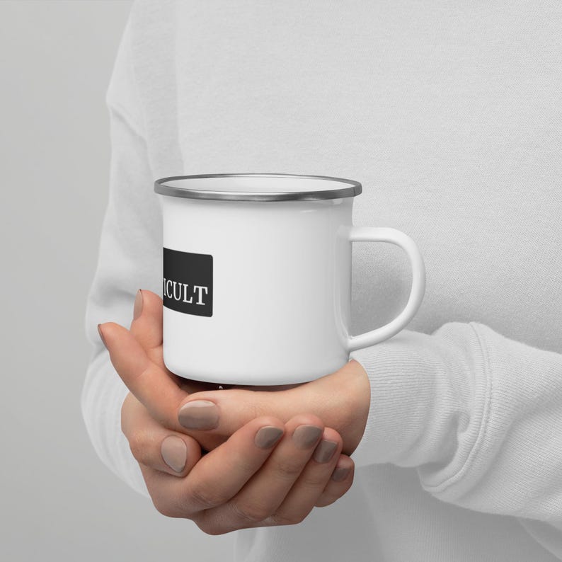May include: White enamel mug with a black rectangle that says "CULT" on it. The mug is being held by a person's hands.