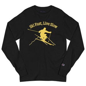 May include: Black long-sleeve t-shirt with a yellow silhouette of a skier on a mountain with the text "Ski Fast, Live Slow".