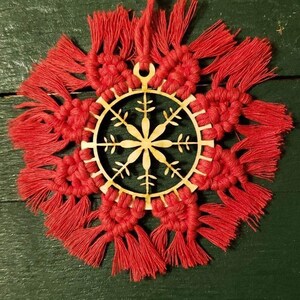 May include: A red and natural wood Christmas ornament featuring a snowflake design. The ornament is decorated with red fringe around the edges.