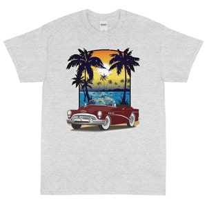 May include: A vintage red convertible car driving on a beach with palm trees and a sunset in the background.