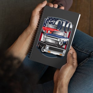 May include: A black spiral notebook with a graphic of three vintage Chevrolet C10 trucks. The trucks are stacked on top of each other and are in different colors: red, blue, and black. The graphic is surrounded by a red, white, and blue American flag design. The text "Chevy C10" is printed in white on the notebook.