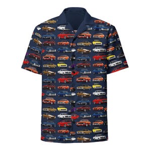 Può includere: Una camicia a maniche corte con bottoni blu navy con un motivo colorato di auto muscolari d'epoca. La camicia presenta una varietà di modelli di auto in diversi colori, tra cui rosso, arancione, giallo, verde, blu e bianco.