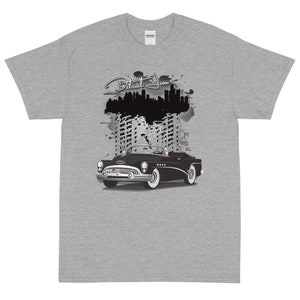 May include: A grey t-shirt with a black and white illustration of a classic car and a cityscape with the text "Detroit Iron" above the car.