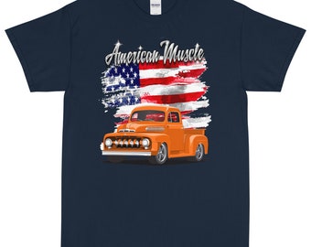 Könnte beinhalten: Ein marineblaues T-Shirt mit einem abgenutzten amerikanischen Flaggen-Design und einem orangefarbenen Vintage-Pickup. Der Text "American Muscle" ist in Silber auf dem Shirt gedruckt.