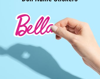 Może przedstawiać: Różowa i biała naklejka z imieniem "Bella" w kursywie. Naklejka jest trzymana przez dłoń na jasnoniebieskim tle. Tekst "Doll Name Stickers" znajduje się nad naklejką.