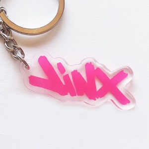 Op de afbeelding: Een roze acryl sleutelhanger met het woord "Yinx" geschreven in een gestileerd lettertype.