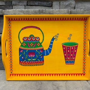 May include: A yellow wooden serving tray with a painted design of a blue and green teapot with a red flower and a green and red cup with steam coming from it.