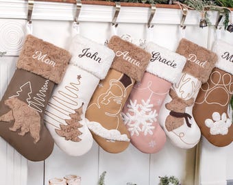 May include: A set of six Christmas stockings in various colors, including brown, white, and pink, each personalized with a name. The stockings feature festive designs like a bear, Christmas tree, snowman, and snowflake, with faux fur cuffs.