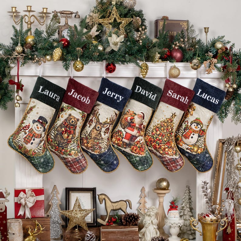 Op de afbeelding: Zes kerstsokken hangen op een rij, elk met een unieke kerstafbeelding zoals een sneeuwpop, beer, hert, kerstman, kerstboom en pingu&iuml;n. Elke sok heeft een gepersonaliseerde naam geborduurd op de donkere boord.