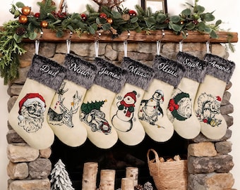 May include: A collection of personalized Christmas stockings hanging above a stone fireplace. Each cream-colored stocking features a different festive design and a name embroidered in cursive. The stockings have a faux fur cuff.