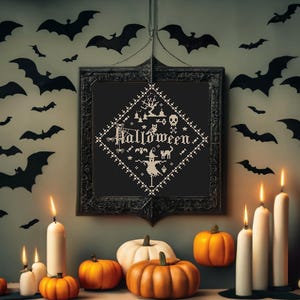 May include: A Halloween-themed display featuring a framed cross-stitch with the word "Halloween", pumpkins, candles, and bat silhouettes. The pumpkins are orange and white, and the candles are lit. The bats are black.
