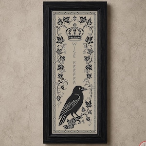 May include: A vertical framed cross-stitch embroidery featuring a black raven perched on a branch, topped with a crown and the text "WISE KEEPER" in black thread on a beige fabric background, surrounded by a decorative black ivy leaf border.
