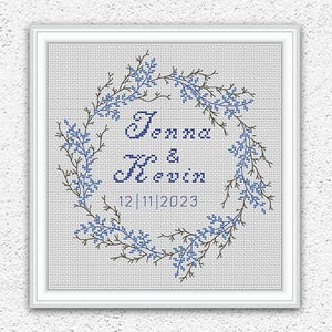 May include: Cross stitch pattern featuring a wreath of blue flowers with the names Jenna & Kevin and the date 12 11 2023 in the center.