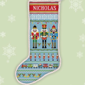 Puede incluir: Patrón de punto de cruz de calcetín navideño azul claro con tres soldados de juguete, un tren y el nombre "NICHOLAS" en rojo. El diseño incluye copos de nieve y el texto "COUNTED CROSS STITCH" e "INSTANT DOWNLOAD PDF".