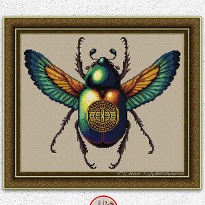 May include: Cross-stitch pattern of a colorful scarab beetle with outstretched wings, framed in a brown wooden border. The beetle features shades of green, blue, and gold. The text "INSTANT DOWNLOAD PDF" is at the bottom.