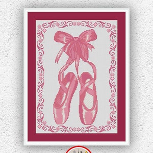 May include: Pink ballet shoes with a pink bow tied on top, framed in a white frame with a red mat. The image is for a cross stitch pattern.