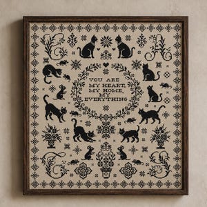 May include: A framed cross-stitch sampler on beige fabric featuring black thread embroidery of various cats, mice, and floral motifs. The central text reads: YOU ARE MY HEART, MY HOME, MY EVERYTHING, surrounded by a decorative wreath and border.