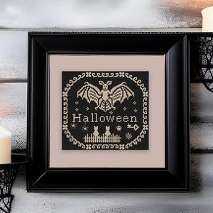 May include: A framed cross-stitch embroidery featuring a black background with cream-colored thread depicting a bat, the word "Halloween", two cats, spiders, and a fence, all enclosed within a decorative border inside a black square frame.