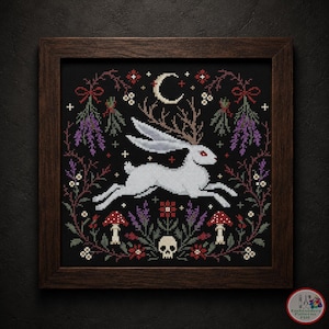 May include: Cross-stitch artwork in a dark wooden frame. The design features a white rabbit with antlers, running across a black background. The design includes a crescent moon, flowers, mushrooms, and a skull. The color palette includes red, purple, and green.