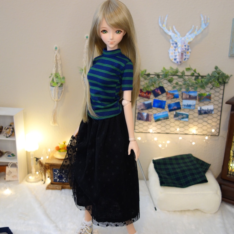 May include: A doll with long blonde hair wearing a blue and green striped shirt and a black tulle skirt with lace trim.