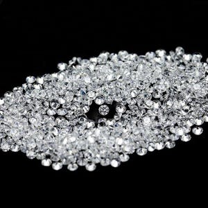 May include: A collection of small, clear, faceted crystals scattered on a black surface. The crystals are round and reflect light, creating a sparkling effect. The crystals are likely used for decoration or crafts.