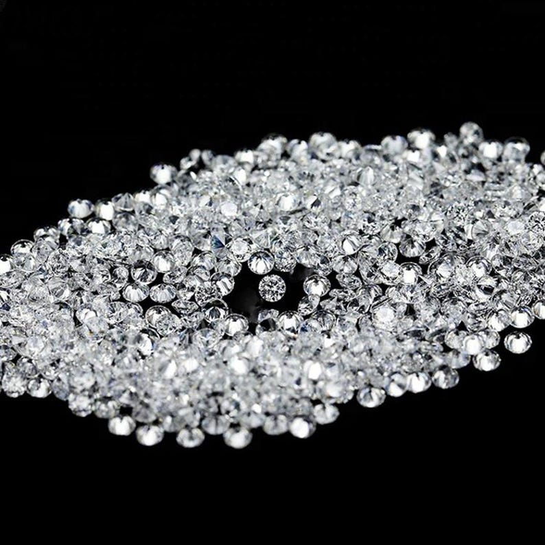 May include: A collection of small, clear, faceted crystals scattered on a black surface. The crystals are round and reflect light, creating a sparkling effect. The crystals are likely used for decoration or crafts.