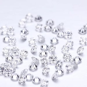 May include: A collection of sparkling, round-cut diamonds scattered across a white surface. The diamonds are clear and reflect light, showcasing their facets. The image highlights the brilliance and clarity of the gemstones, suggesting their use in jewelry or other decorative applications.