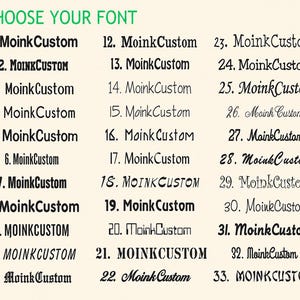K&ouml;nnte beinhalten: Eine Schriftart-Auswahltabelle mit der &Uuml;berschrift CHOOSE YOUR FONT, die 33 nummerierte Optionen des Textes MoinkCustom in verschiedenen schwarzen Schriftarten zeigt, von fetten serifenlosen und Serifenschriften bis hin zu dekorativen, kursiven und stilisierten Designs.