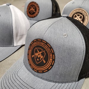May include: Three gray and black trucker hats with a brown leather patch that says "Defensive Strategies and Firearms, LLC" with a shield and crossed rifles inside the patch.