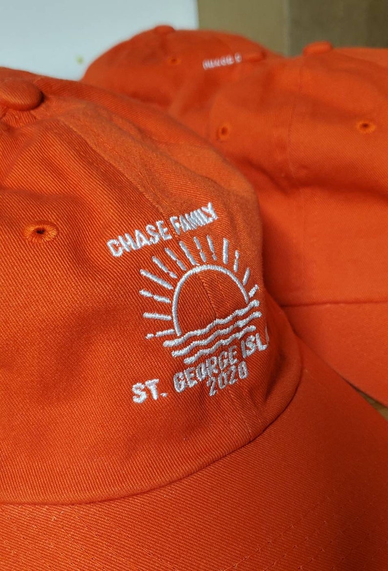 May include: Bright orange baseball caps with white embroidered text and a sun and water design. The text reads "CHASE FAMILY", "ST. GEORGE ISL" and "2020". The caps are made of a durable fabric.