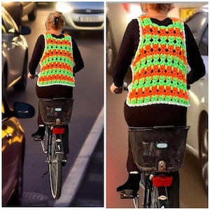 以下が含まれることがあります： 自転車に乗っている人が、手作りのかぎ針編みのベストを着ています。 ベストはオレンジと緑の鮮やかな模様で、白で縁取られています。 自転車には黒いバスケットと赤いリフレクターが付いています。