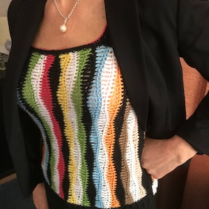 Może przedstawiać: Kobieta w czarnym blazerze, na którym nosi kolorowy, pasiasty top na szydełku. Top ma różne kolory, w tym czerwony, pomarańczowy, żółty, zielony, niebieski i brązowy.